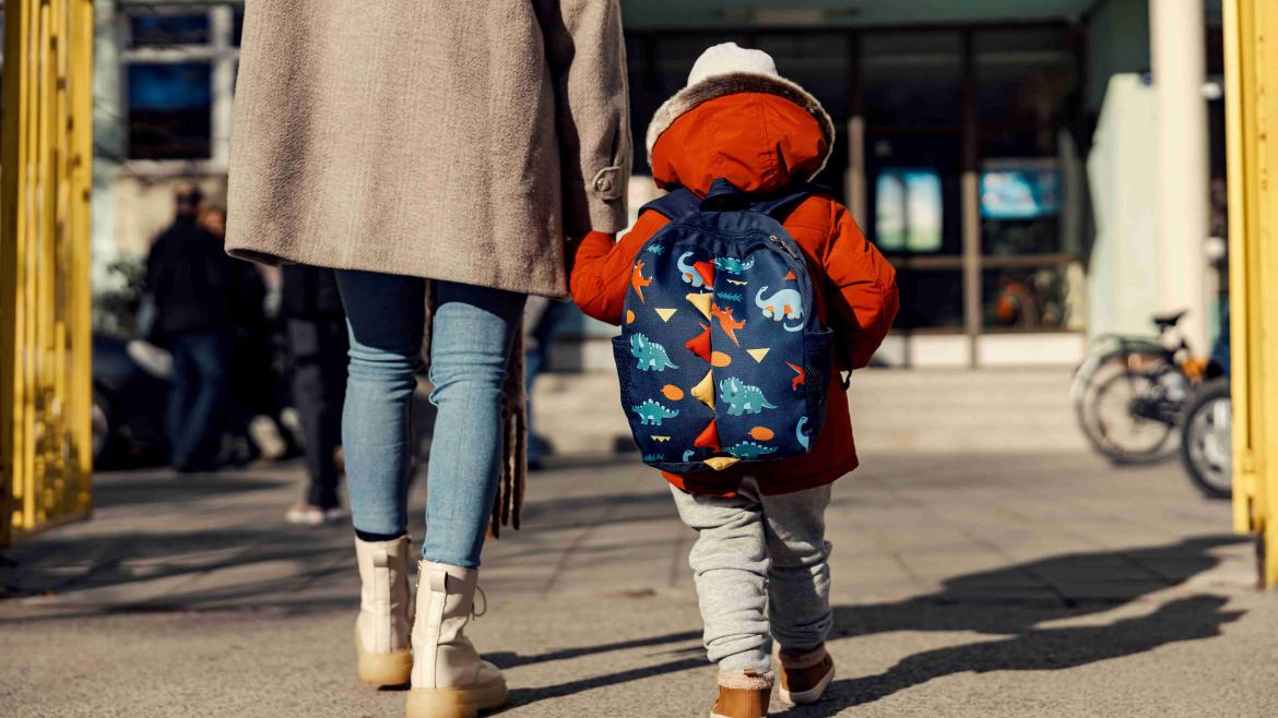 Kind läuft an der Hand mit Rucksack auf in die Kita