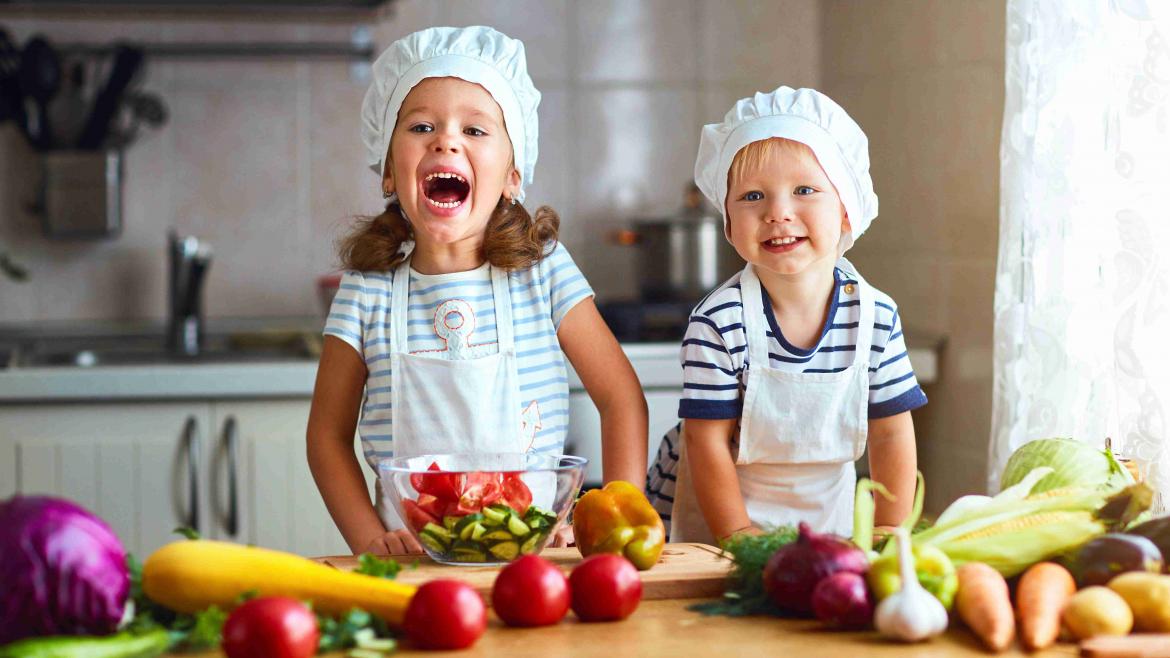 Zwei Kinder in der Küche mit Schürzen und Kochhauben