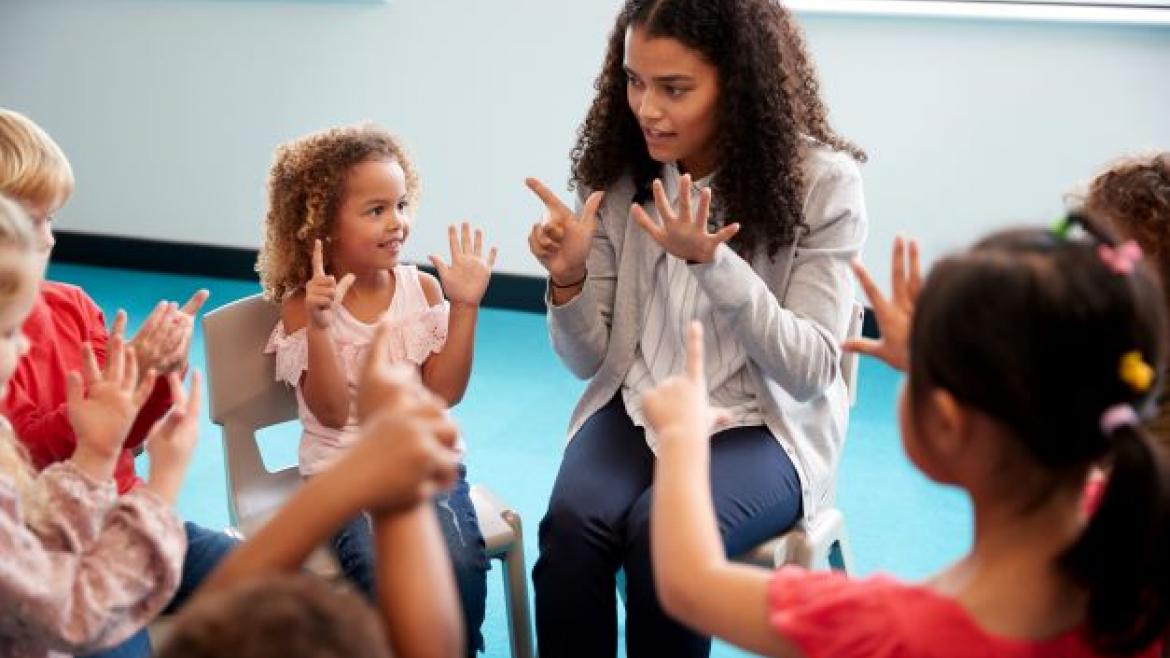 Erziherein sitzt mit Kindern im Stuhlkreis und übt zählen mit den Fingern.
