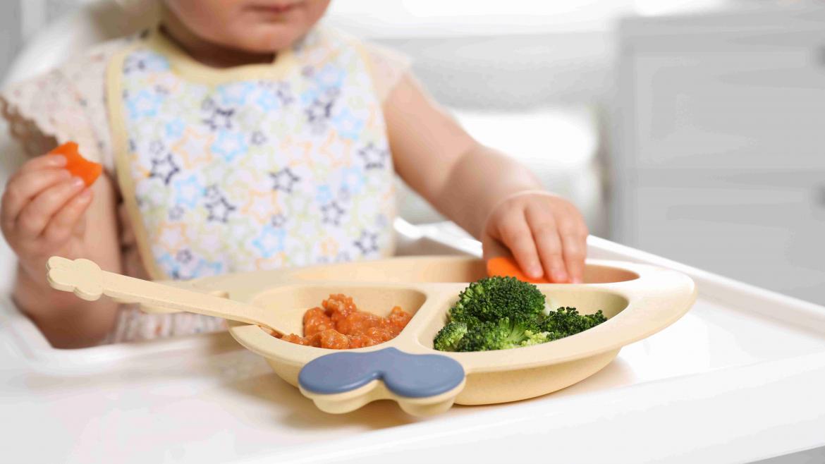 Kind istt mit Händen aus einem Kindertelller Gemüse