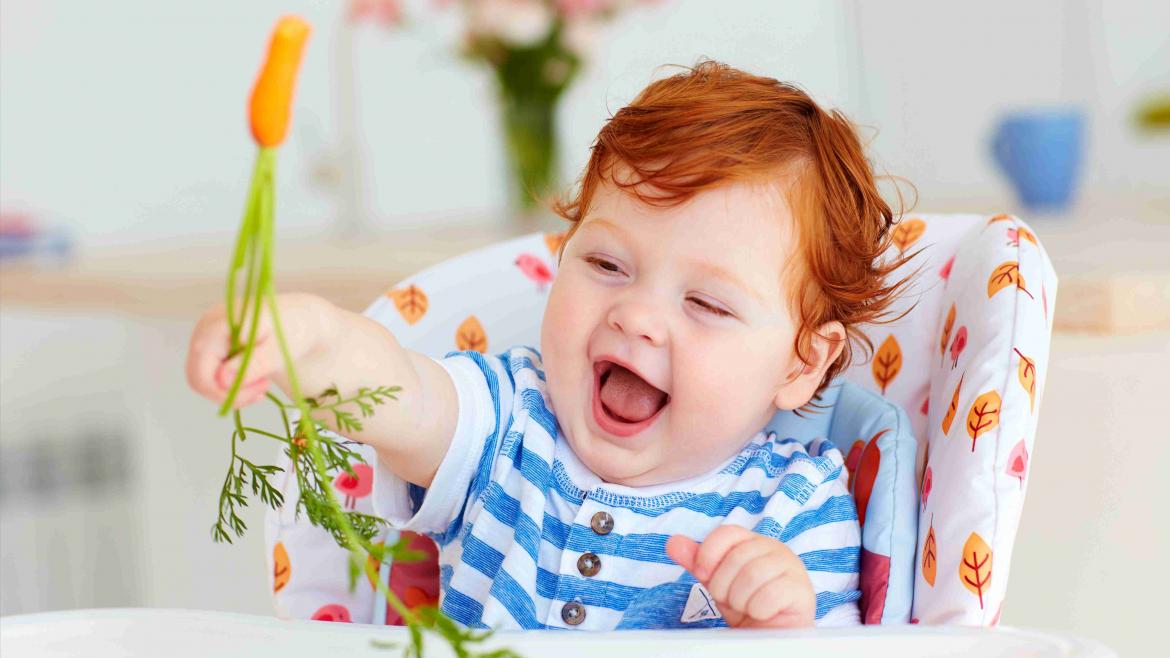 Kind mit roten Haaren lacht und hat eine Möhre mit Möhrengrün in der Hand