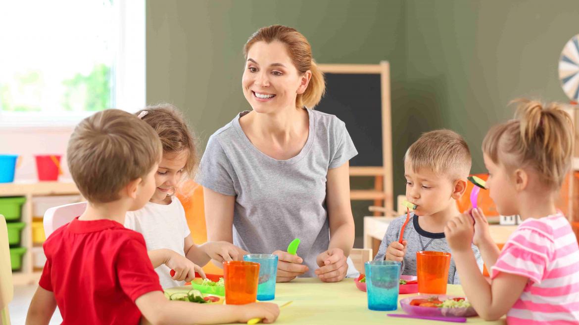 Erzieherrin sitzt mit Kindern am Tisch