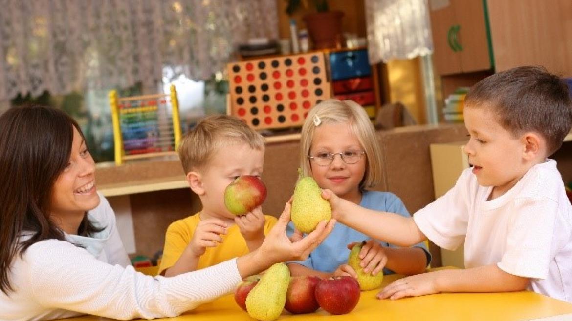 Erzeiherin am Tisch mit Kindern die Äpfel und Birenen in der Hand halten