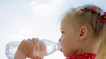 Kind trinkt im freien aus einer Wasserflasche. Im Hintergrund ist der Himmel zu sehen.