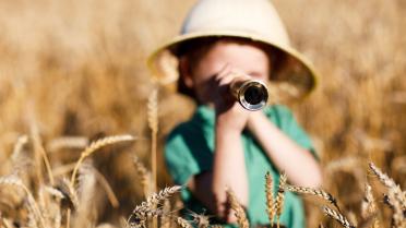 Kind steht mit Fernrohr im Kornfeld