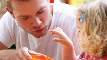 Kind und Kitaerzieher - Kind isst aus einer orangenen Schüssel