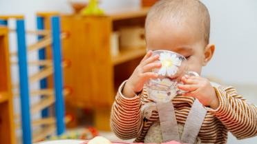 Kleinkind trinkt aus Tasse am Tisch in der Kita