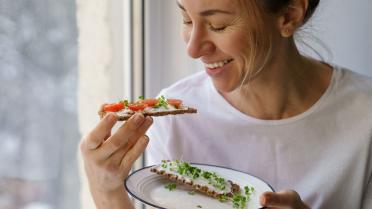 Frau hat eine belegtes Brot in der Hand und lächelt
