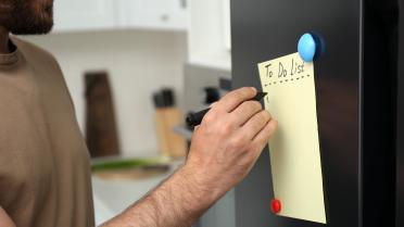 Mann schreibt eine To Do Liste. Er ist nur halb im Bild zu sehen.
