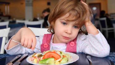 Kind sitzt lustlos vorm Teller voller Essen