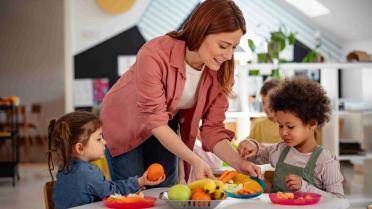 Obst und Gemüse in der Kita auf einem Tisch, zwei Kinder und Erzieherin