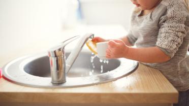 Kind wäscht Tasse üver rundem Waschbecken ab