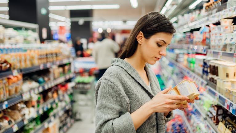 Frau im Supermarkt schaut sich den Nutri Score auf einer Verpackung an