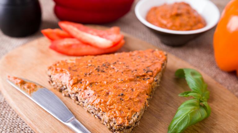 Brot mit Tomatenaufstrcih im Vordergrund. Im Hintergrund eine Schale des Tomatenaufstrichs, Basilikum, eine frische Tomate