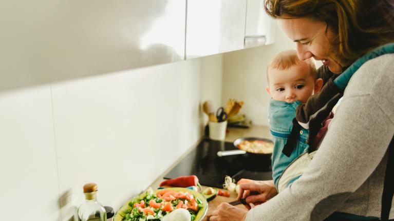 Frau mit Baby in Trage in der Küche