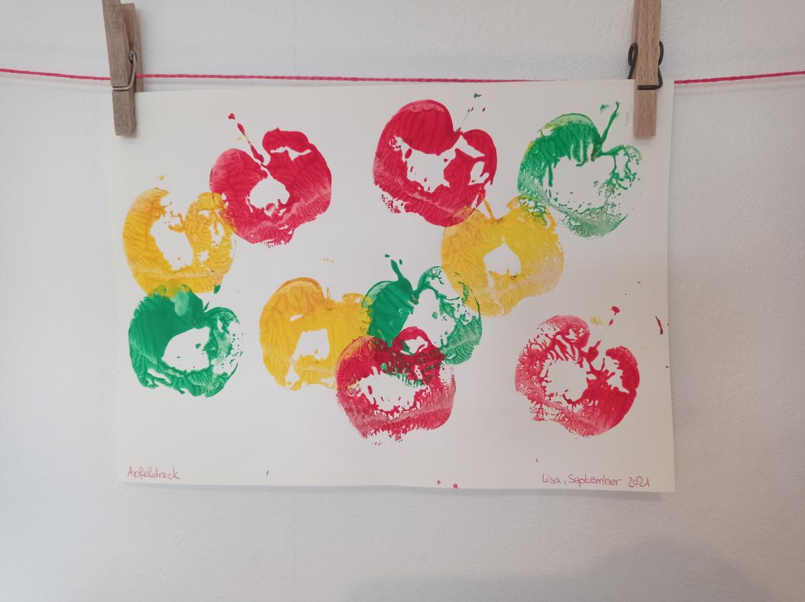 Gestempelte Äpfel auf einem Blatt Papier an einer Wäscheleine in den Farben gelb, grün, rot