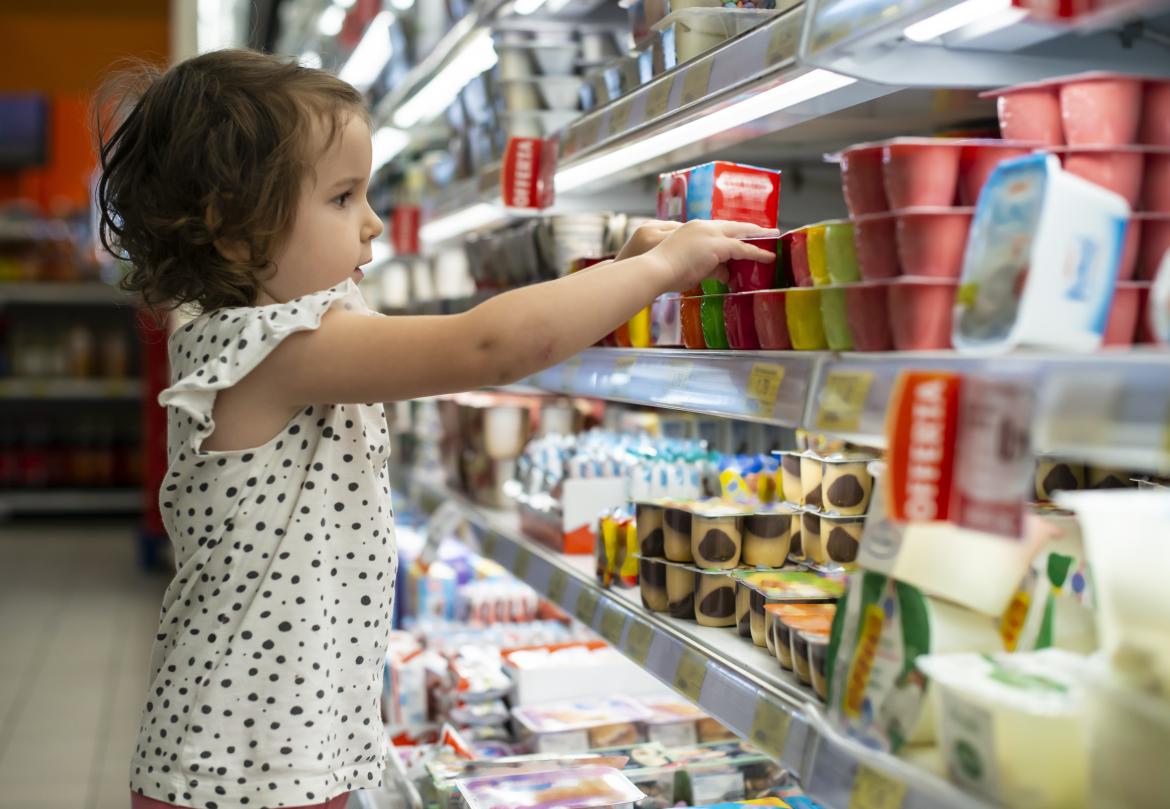 Kind steht seitlich vor Supermarktregal und greift nach Fruchtzwergen