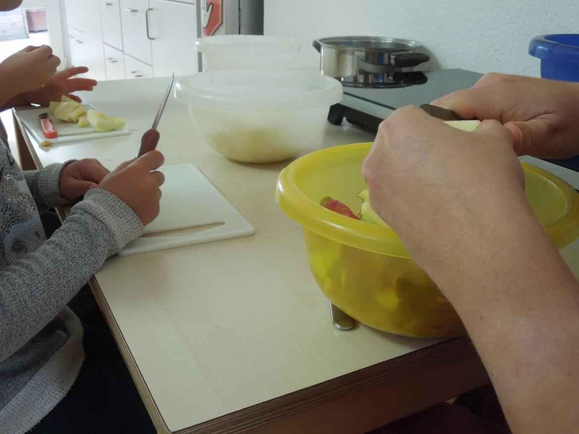 Mehrere Kinder sitzen am Tisch und schneiden Äpfel klein. Man sieht ihre Gesichter nicht.