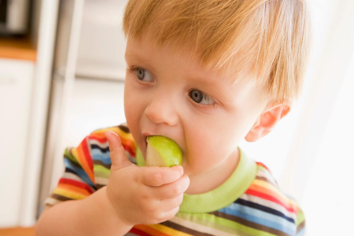 Kleiner Junge hat ein Stück Apfel im Mund
