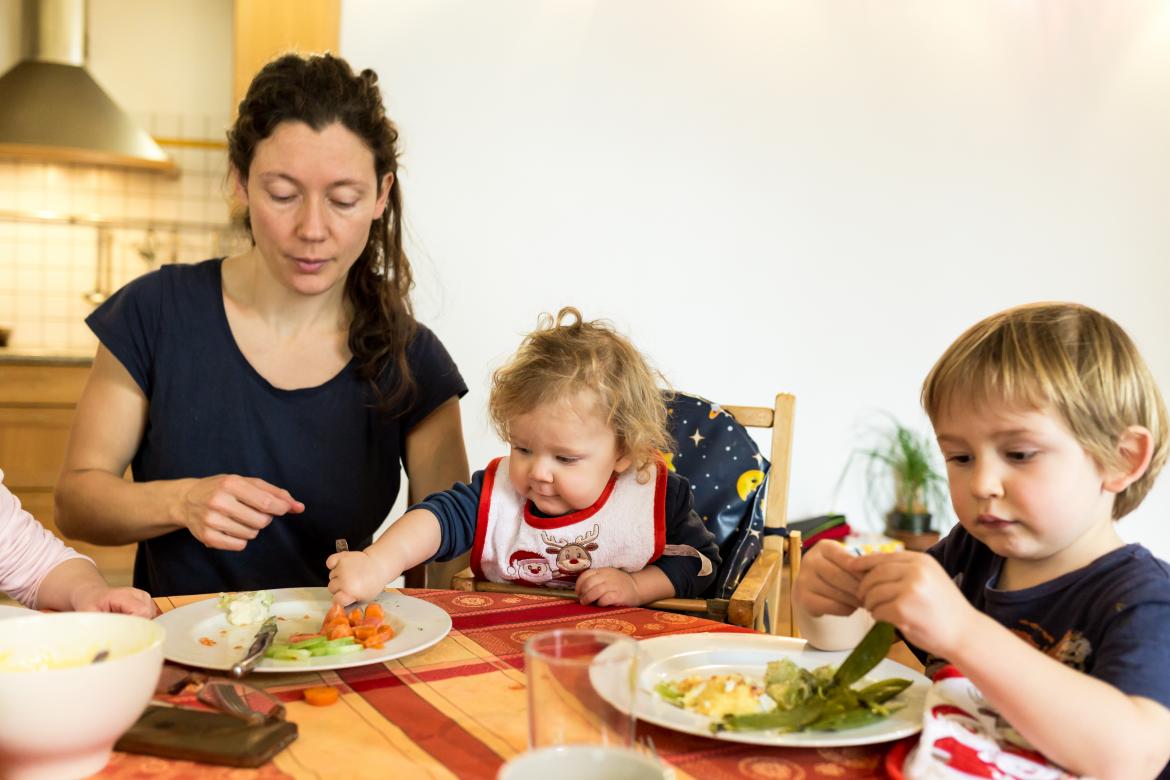 Kinder essen mit Erzieherin am Tisch