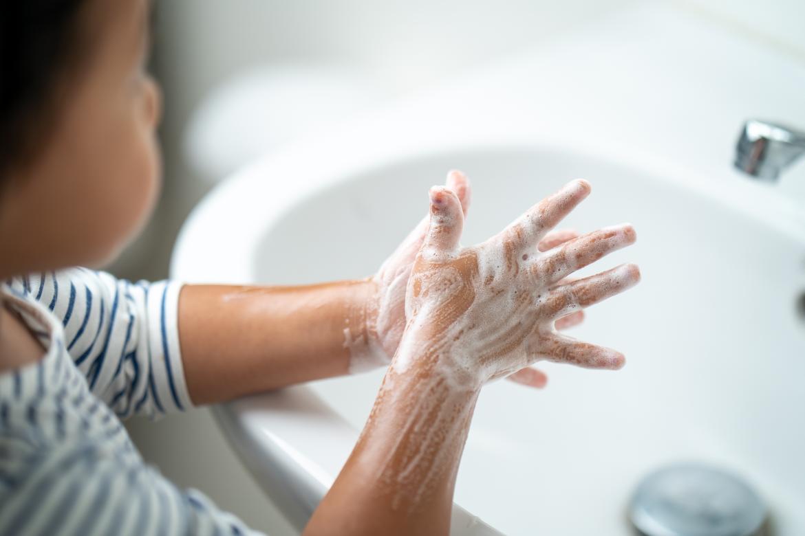 Kind wäscht sich die Hände mit Seife über Waschbecken