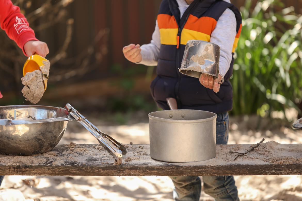 Jungs spielen draußen mit Kochtöpfen und Sand. Ihre Köpfe sind nicht zu sehen.