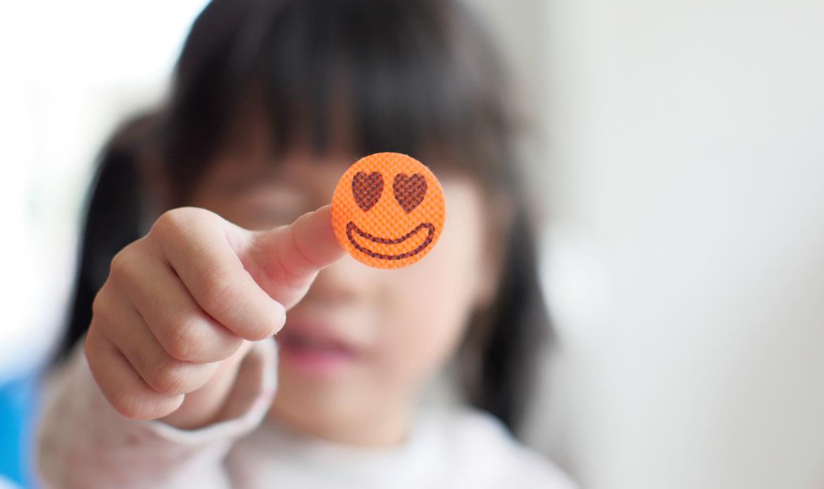 Kind hält kleine Waffel in die Kamera, Auf der Waffel ist ein Smilygesicht zu sehen.