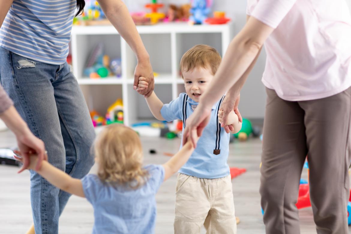 Zwei Kinder in der Kita an der Hand von Erzieherinnen