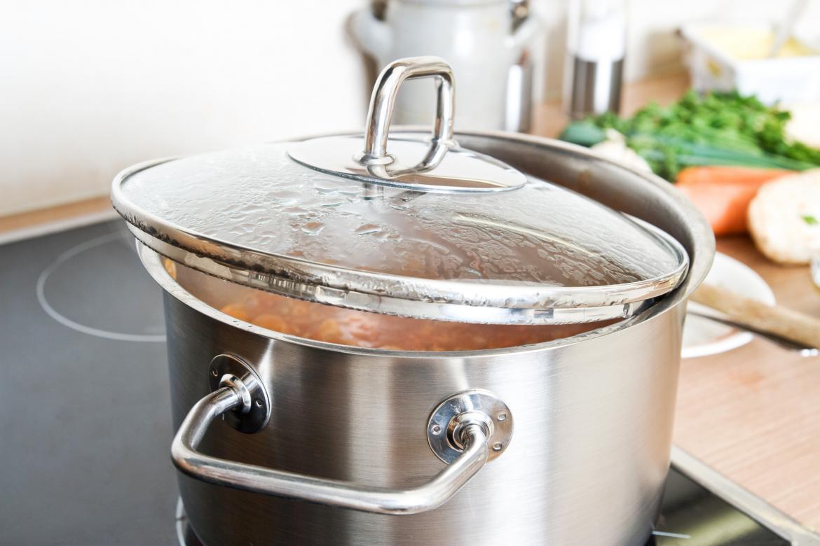 Kochtopf mit Deckel der halb auf dem Topf ist. Der Deckel ist angelaufen, im Topf befindet sich eine rote Suppe