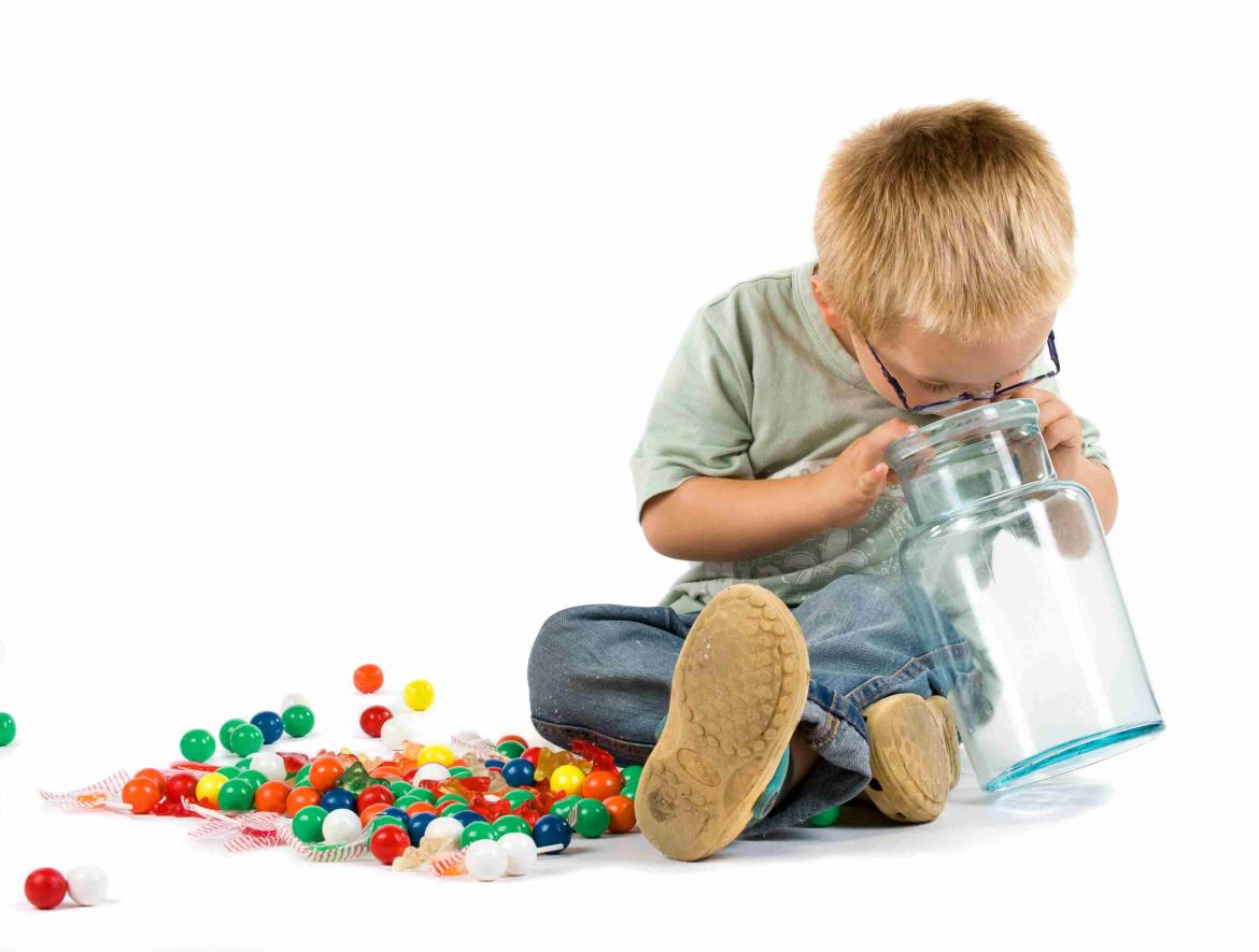 Kind schaut in ein leeres Glas neben ihm bunte Zuckerschokoladenkugeln