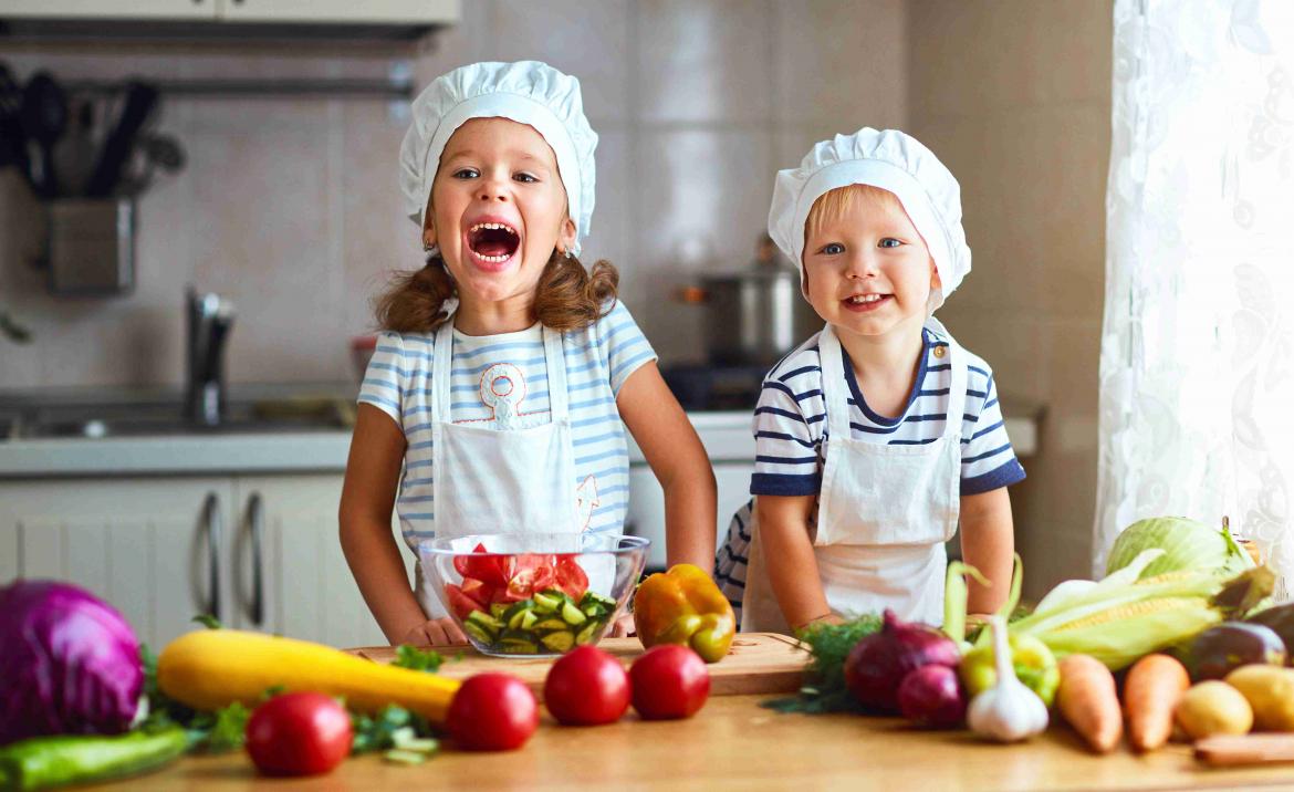 Zwei Kinder in der Küche mit Schürzen und Kochhauben