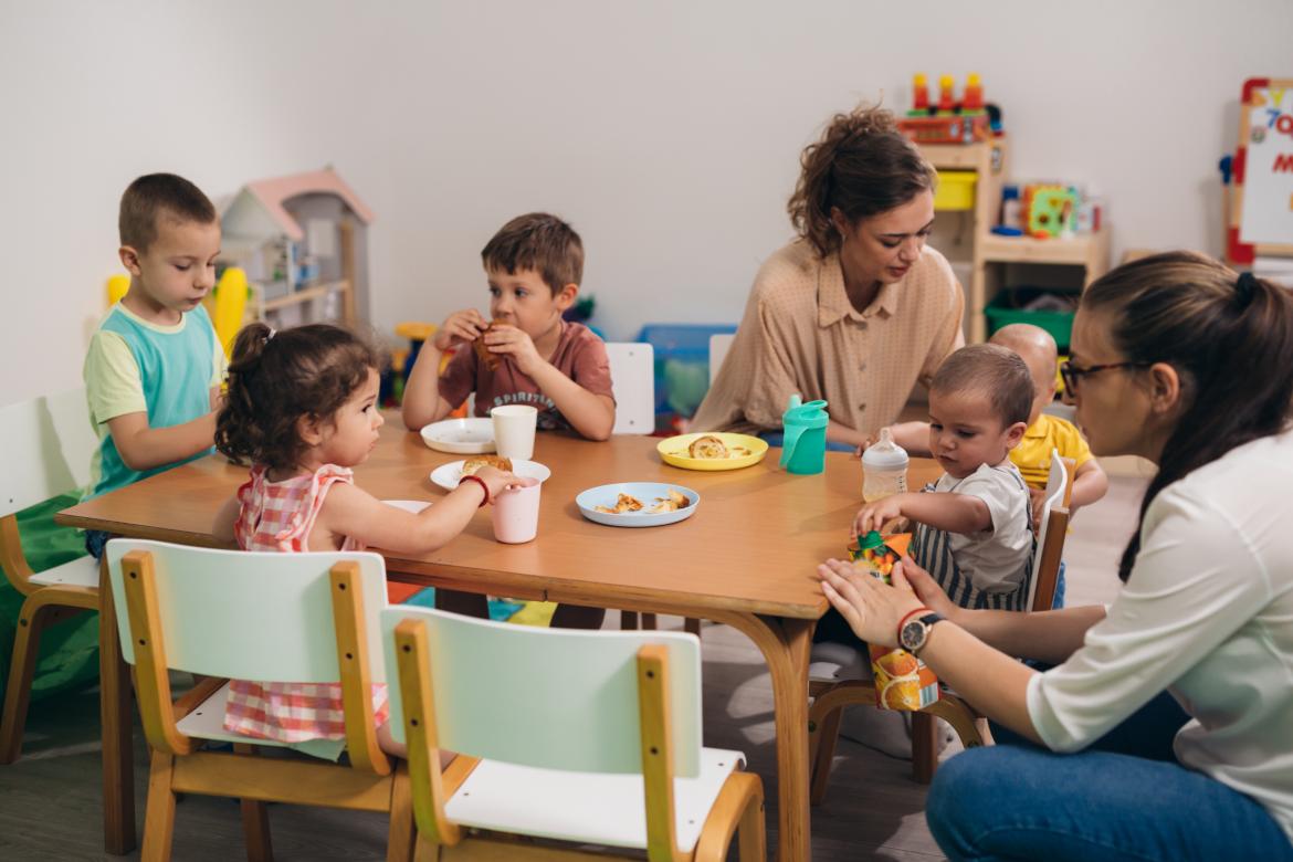 Kinder essen in der Kita mit Erzieherinnen am Tisch