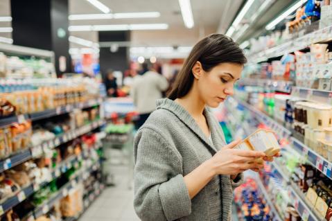 Frau im Supermarkt schaut sich den Nutri Score auf einer Verpackung an
