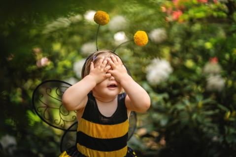 Kind im Bienenkostüm steht im Garten und hält sich die Augen zu.