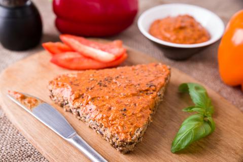 Brot mit Tomatenaufstrcih im Vordergrund. Im Hintergrund eine Schale des Tomatenaufstrichs, Basilikum, eine frische Tomate