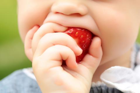 Kind beisst in eine rote Erdbeere