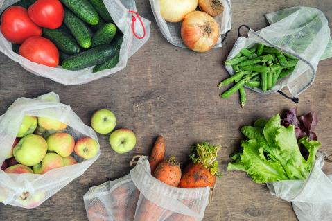 Meherere durchsichtige Stoffbeutel liegen in einem Kreis, sie beinhalten verschiedene Gemüsesorten wie Gurken, Tomaten, Möhren