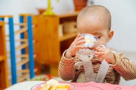 Kleinkind trinkt aus Tasse am Tisch in der Kita