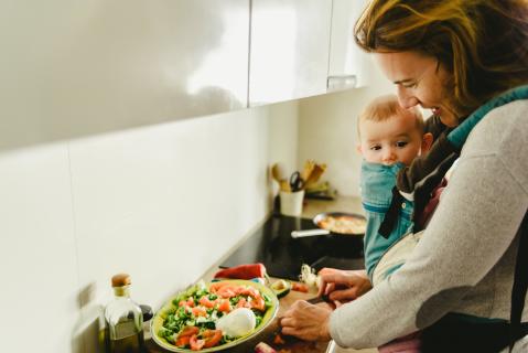 Frau mit Baby in Trage in der Küche